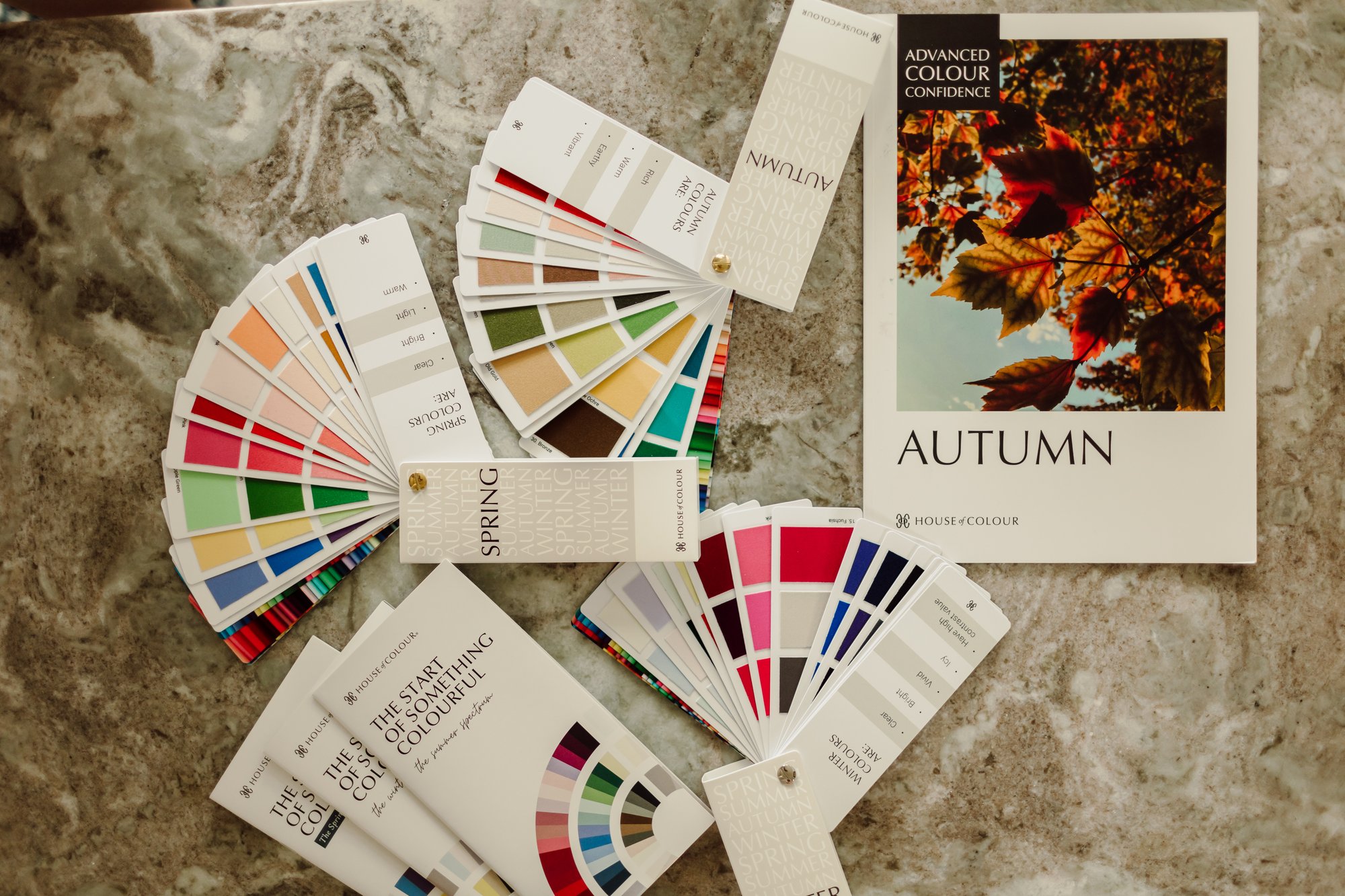 Flat lay of House of Colour swatch fans and an Autumn color guide on a marble table