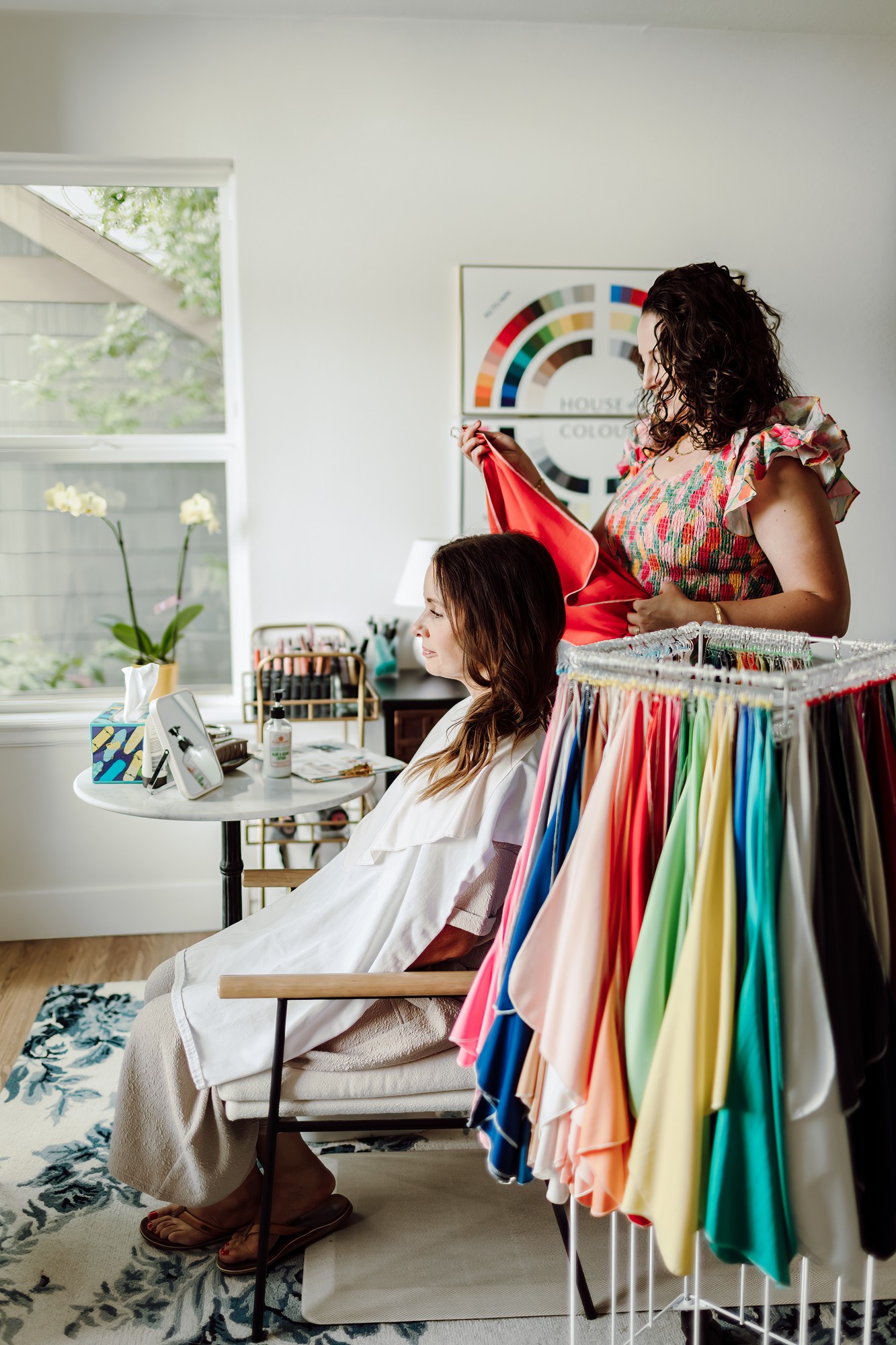Client seated in a styling studio as the consultant holds up a coral drape, a rainbow of color drapes on a rack between them