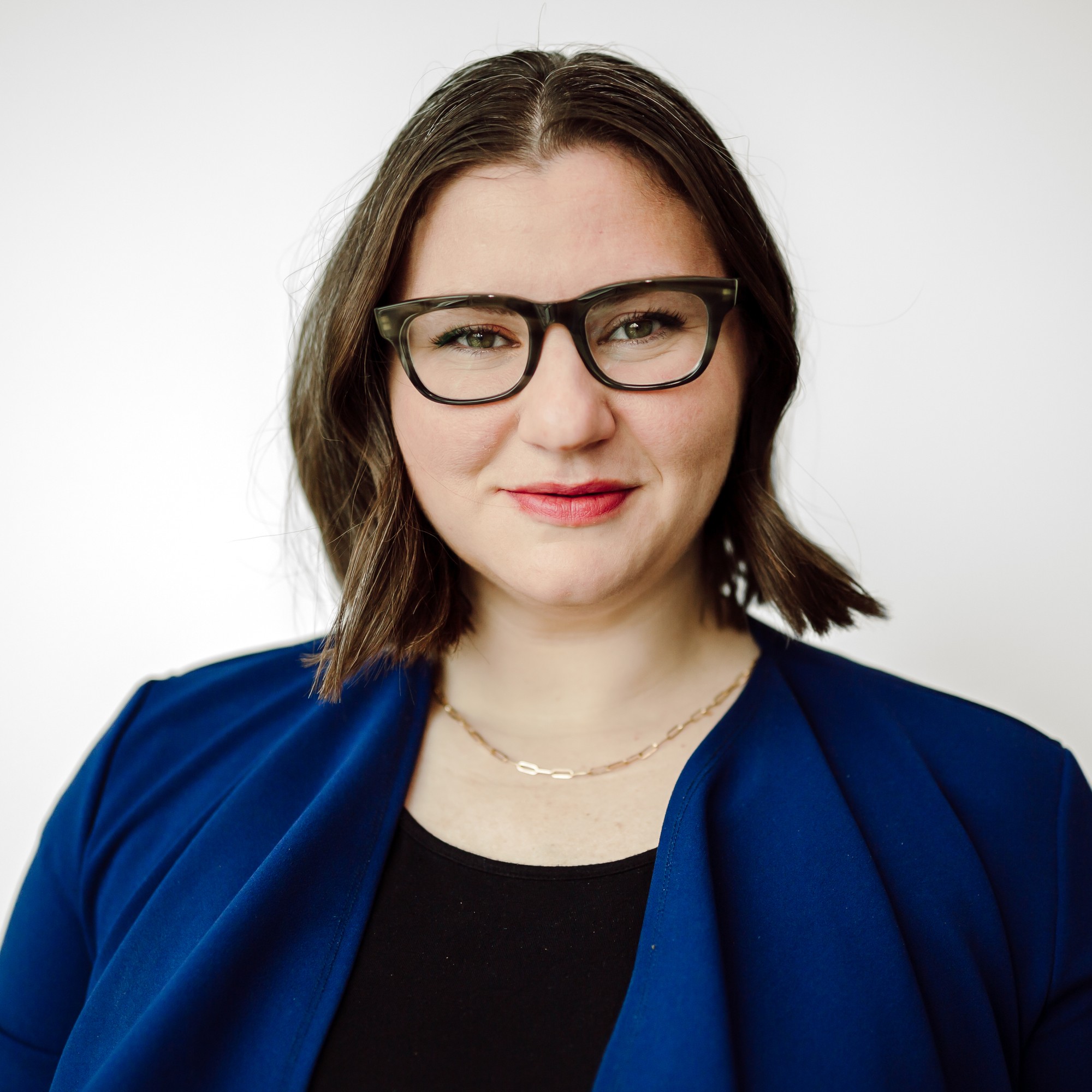 Corporate headshot of a team member in dark-rimmed glasses and a blue jacket
