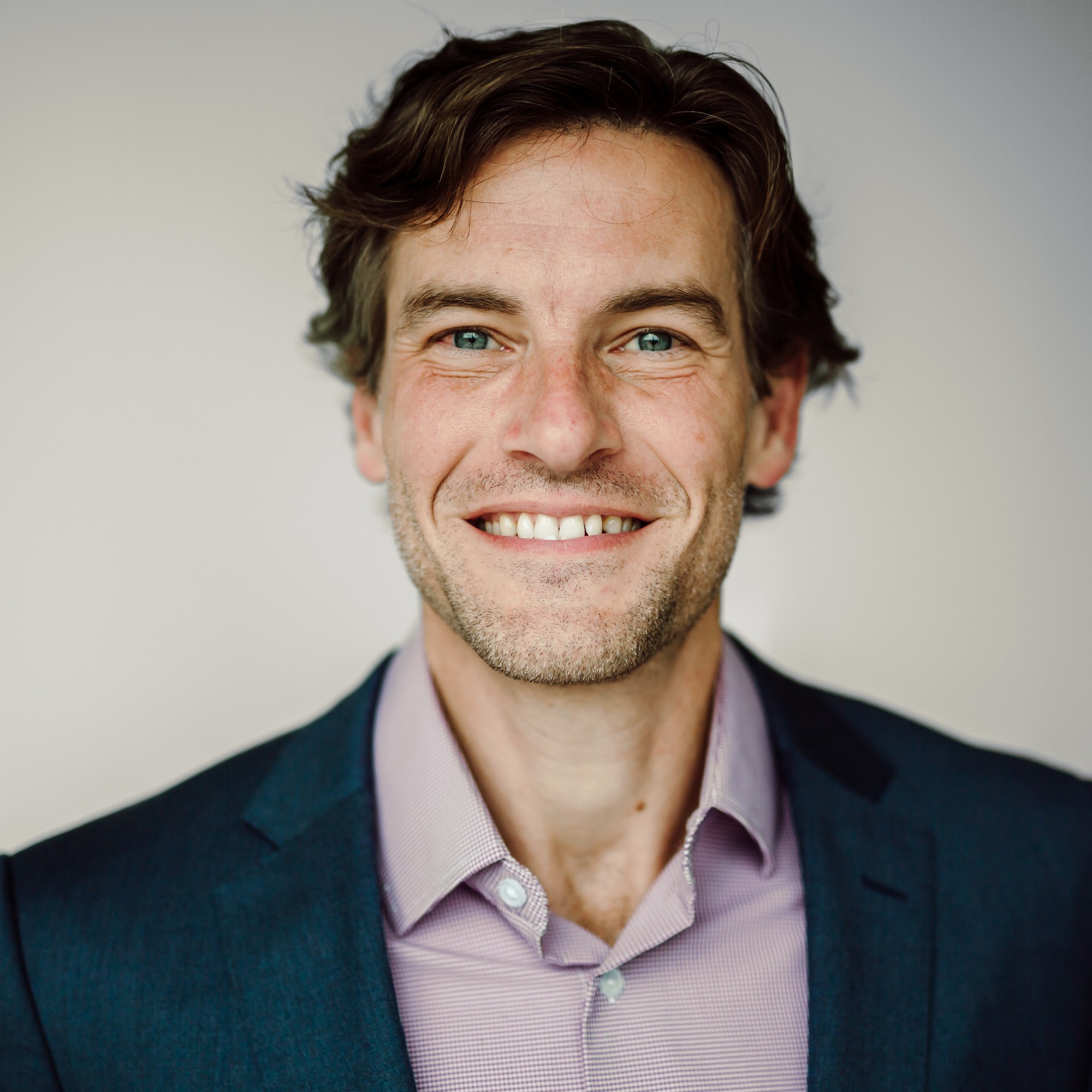 Corporate headshot of a team member in a navy blazer and checked shirt