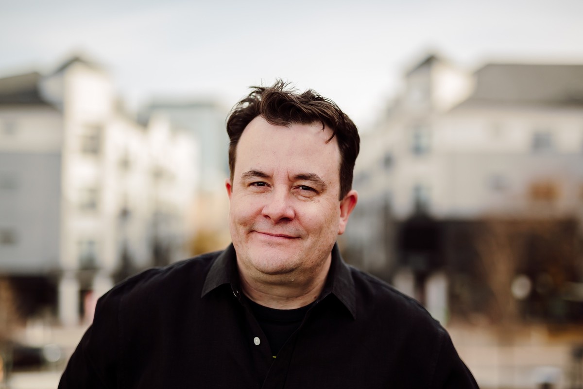 Client in a black button-up shirt, smiling in front of softly blurred city buildings