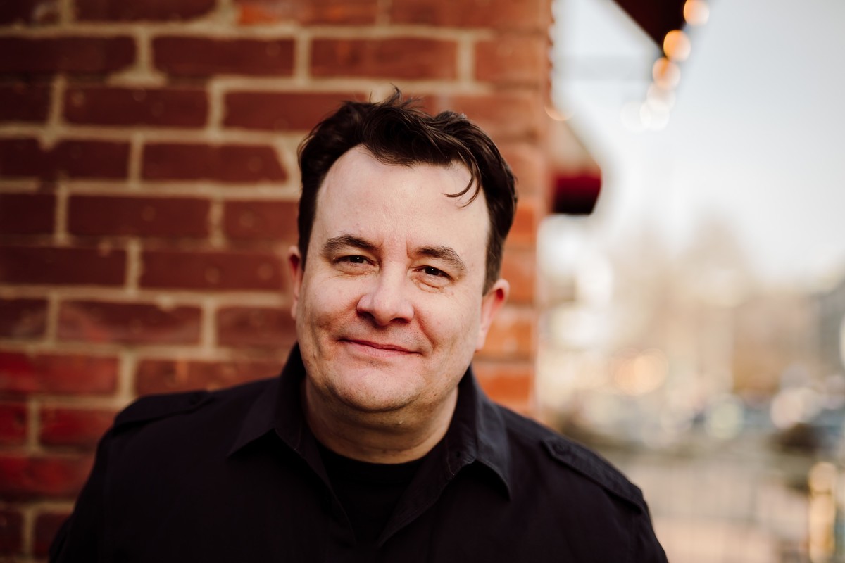 The same client in a dark shirt beside a red brick wall