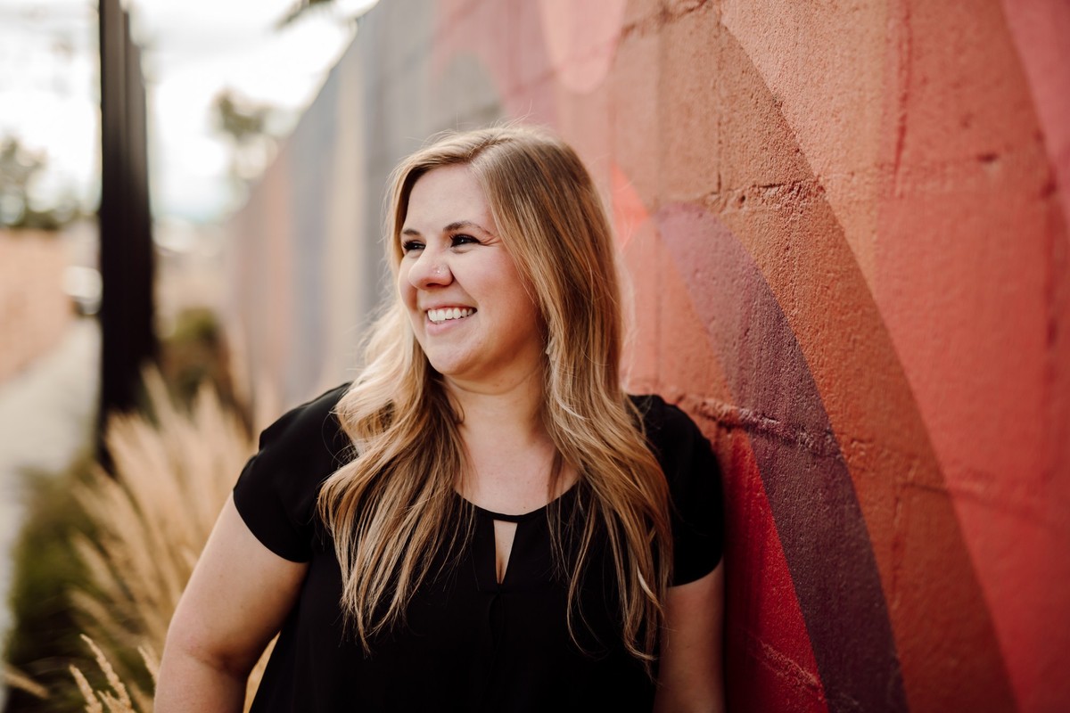 Client with long blonde hair laughing and looking away, leaning on a red mural wall