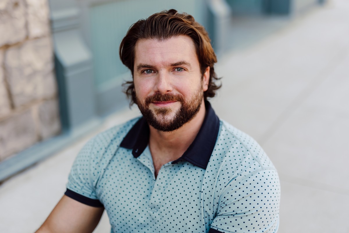 Client in a light blue polka-dot polo with a navy collar, seated on a sunny sidewalk