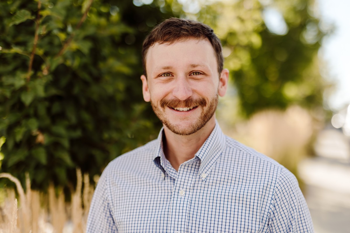 Client in a blue checked shirt smiling in front of sunlit greenery