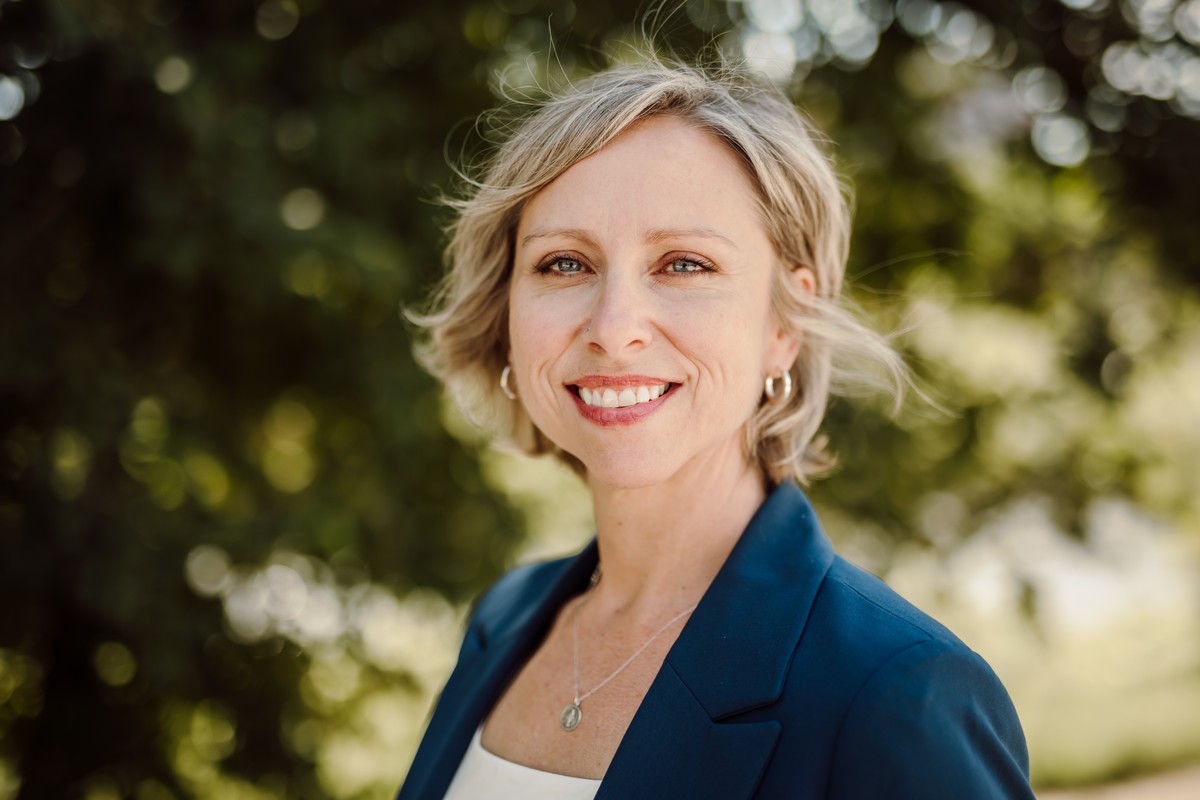 The same client in a blue blazer, photographed outdoors among trees