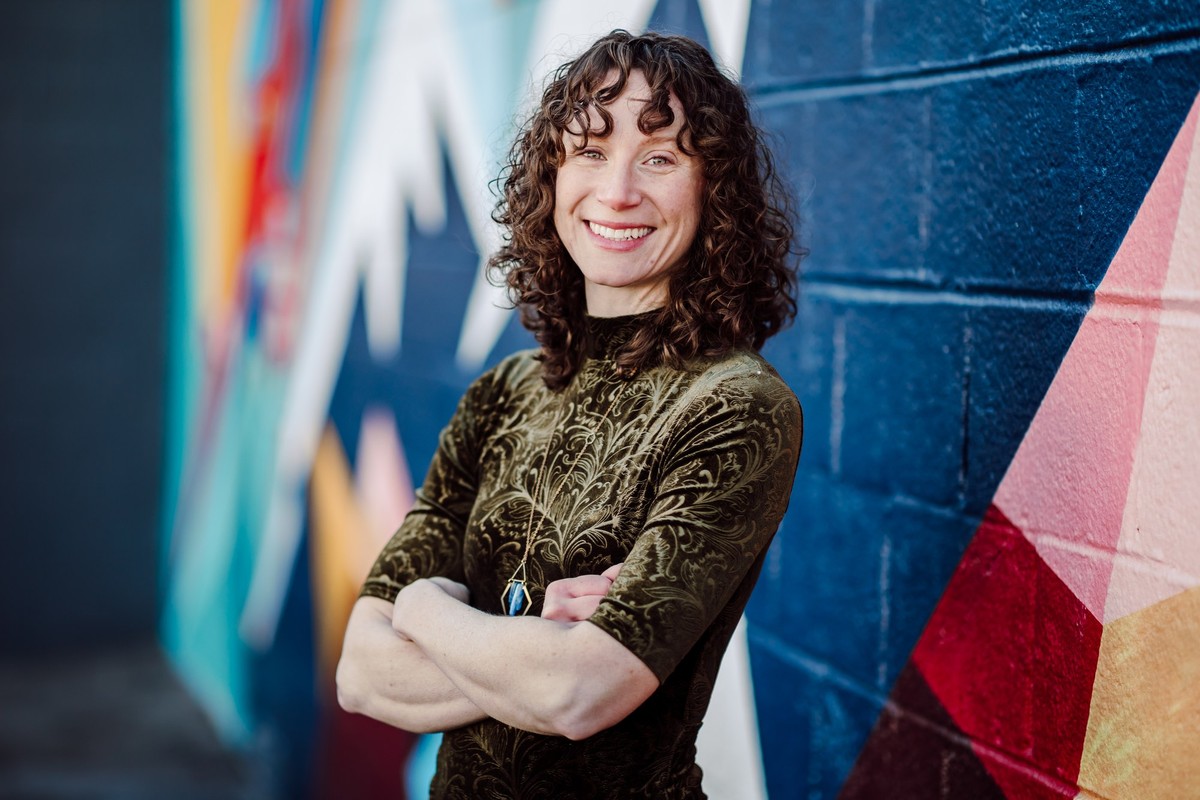 Client in an olive velvet top, arms crossed in front of a colorful mountain mural