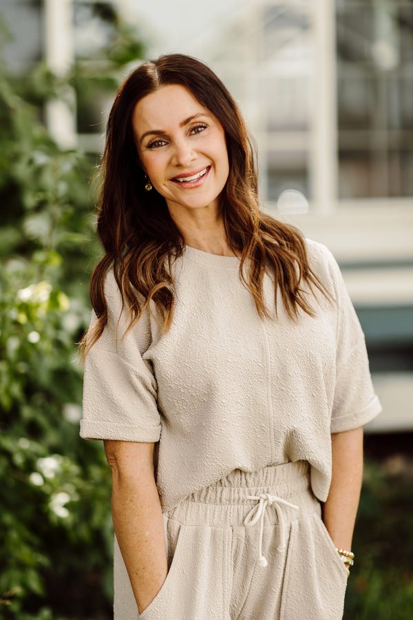 Headshot client in a textured beige outfit, smiling outdoors beside a garden