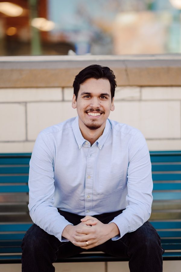 Headshot client in a light blue button-down shirt, seated on a teal bench downtown