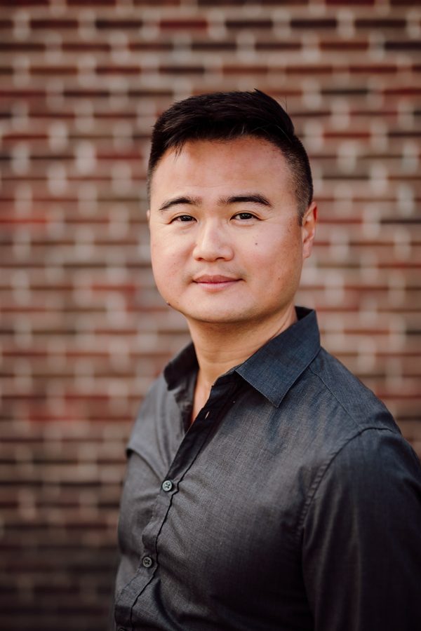 Headshot client in a grey button-down shirt against a brick wall
