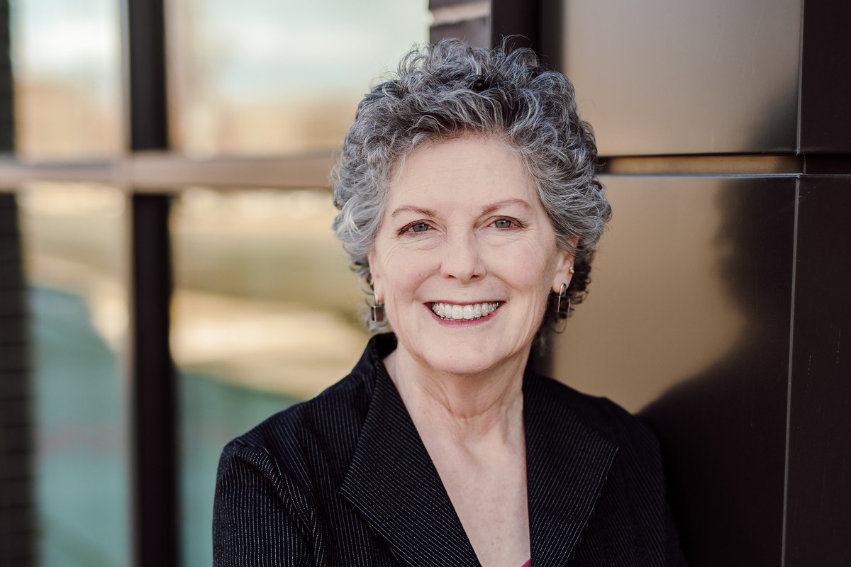 Headshot client with silver curls in a black pinstripe blazer, smiling outside an office building
