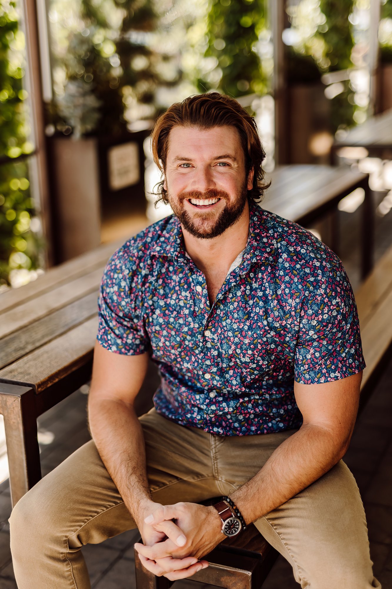 Headshot client in a floral shirt laughing on a sunny patio bench